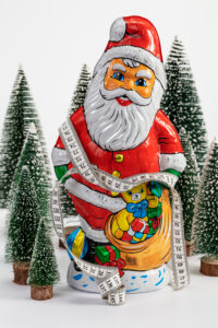 Tape measure wrapped around chocolate Santa Claus, stands in the midst of miniature Christmas trees, white background, icon image, Christmas time, slimming, Tape measure wrapped around chocolate Santa Claus, stands in the midst of miniature Christmas trees, white background, icon image, Christmas time, slimming,